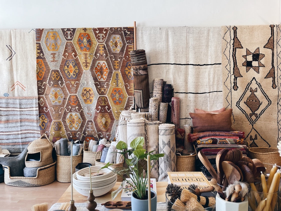 vintage rugs hanging from a wall rack with more rugs rolled and stacked