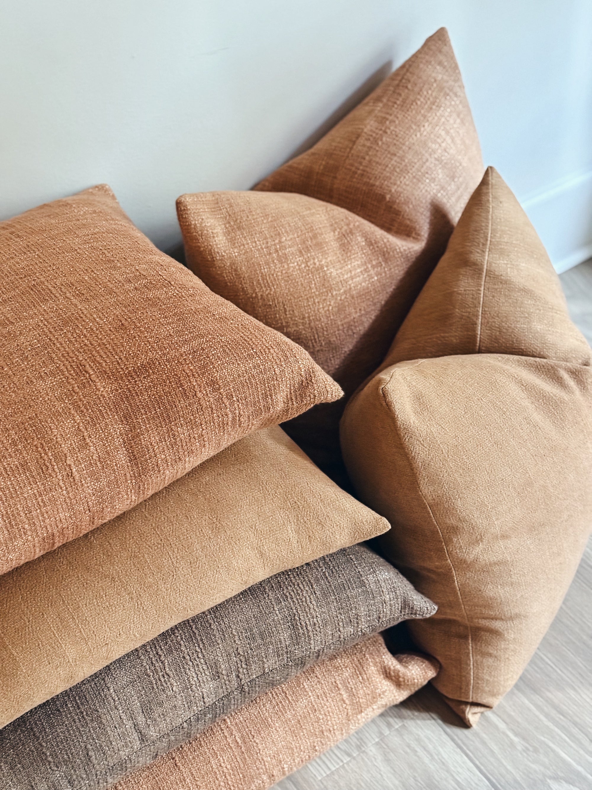 Stack of earth tone textured pillows on a light wooden floor.