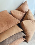 Stack of earth tone textured pillows on a light wooden floor.